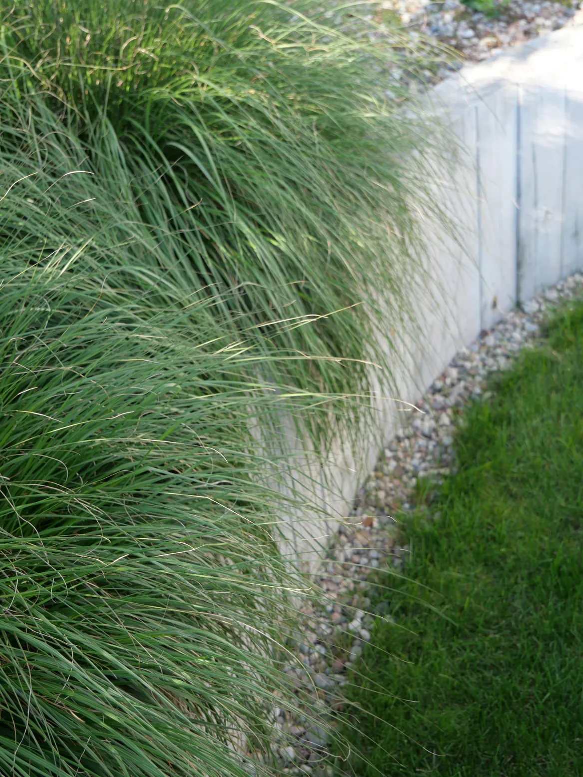 Drewniany mur oporowy ze żwirową opaską przy domu.