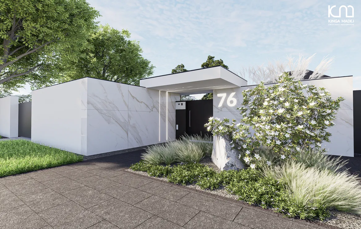 Widok furtkę wejściową. Ogrodzenie frontowe betonowe obłożone spiekiem kwarcowym. Rabata z magnolią gwieździstą, stipami barwinkiem.