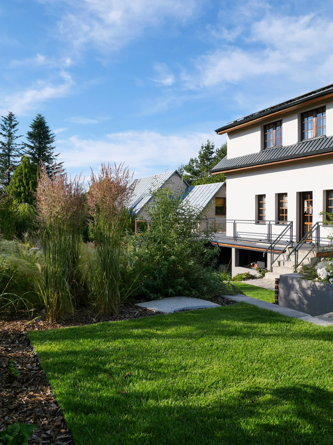 Trawnik na najwyższym piętrze ogrodu. Rabata z trawiasto-bylinowa ściółkowana korą.